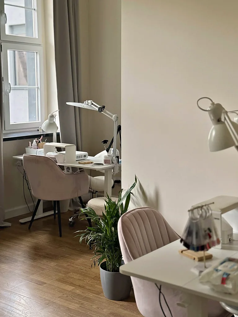 Wnętrze studia: stanowisko do manicure przy oknie kamienicy, pudrowy fotel i roślina